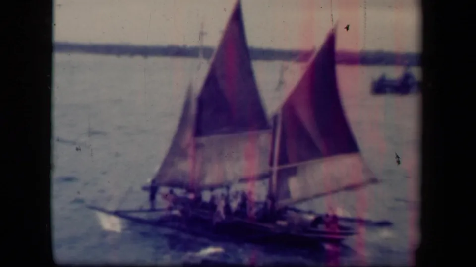 A traditional sailboat with faded red and purple sails passes through Leyte Gulf water, carrying several visible passengers.