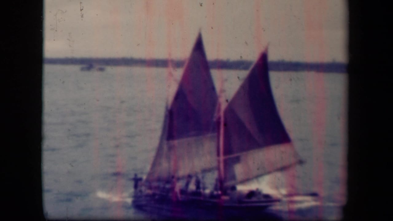 1944 Leyte Gulf 8mm frame showing a small sailing craft with two triangular sails and people aboard on open water.