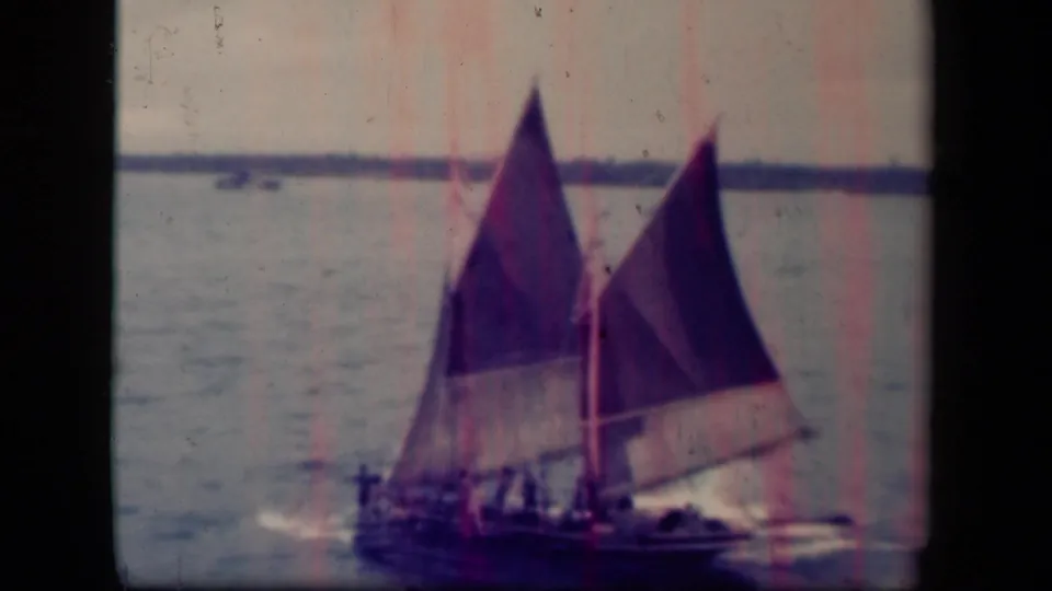 1944 Leyte Gulf 8mm frame showing a small sailing craft with two triangular sails and people aboard on open water.