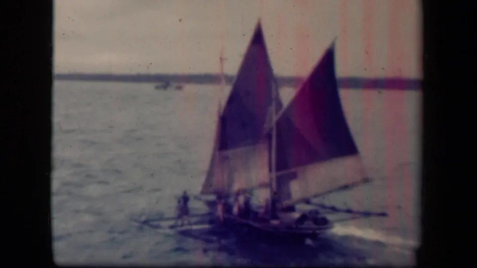 Closer 8mm view of the Leyte Gulf sailing craft, with people clustered near the center and a wake trailing beside the hull.