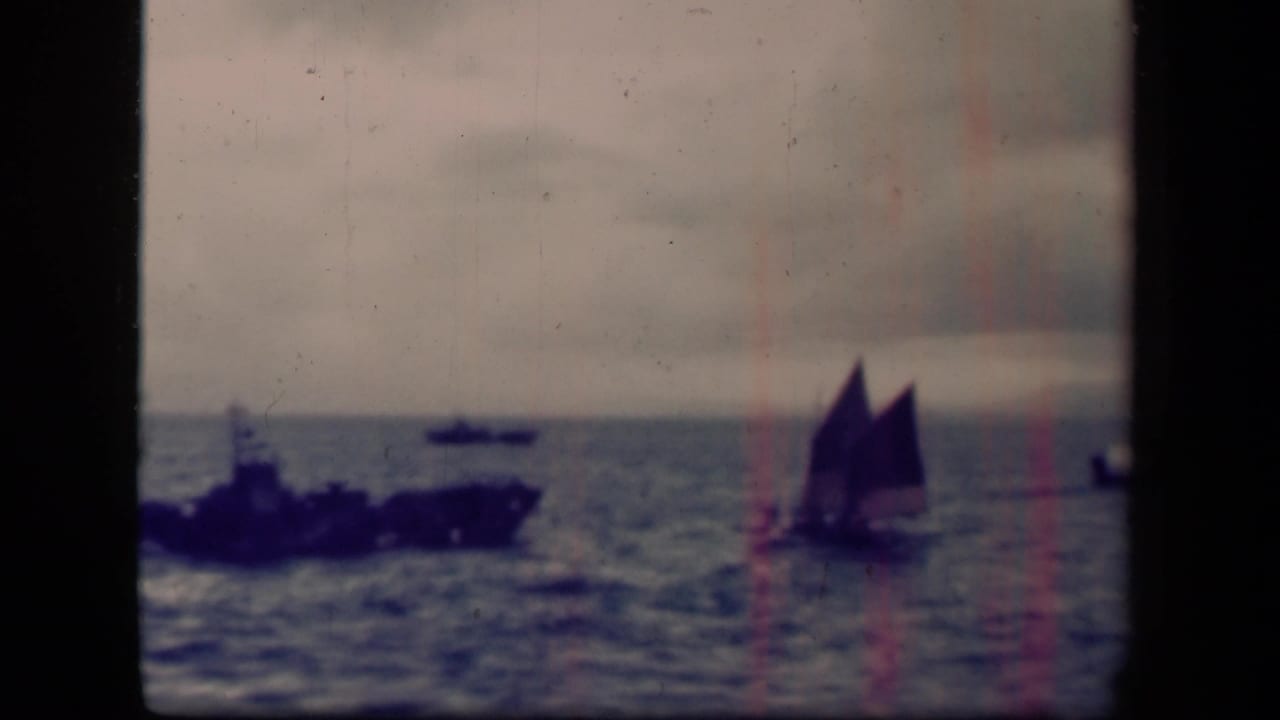 Leyte Gulf 1944 8mm frame showing a distant dark warship at left and a small sailboat at right on the ocean.