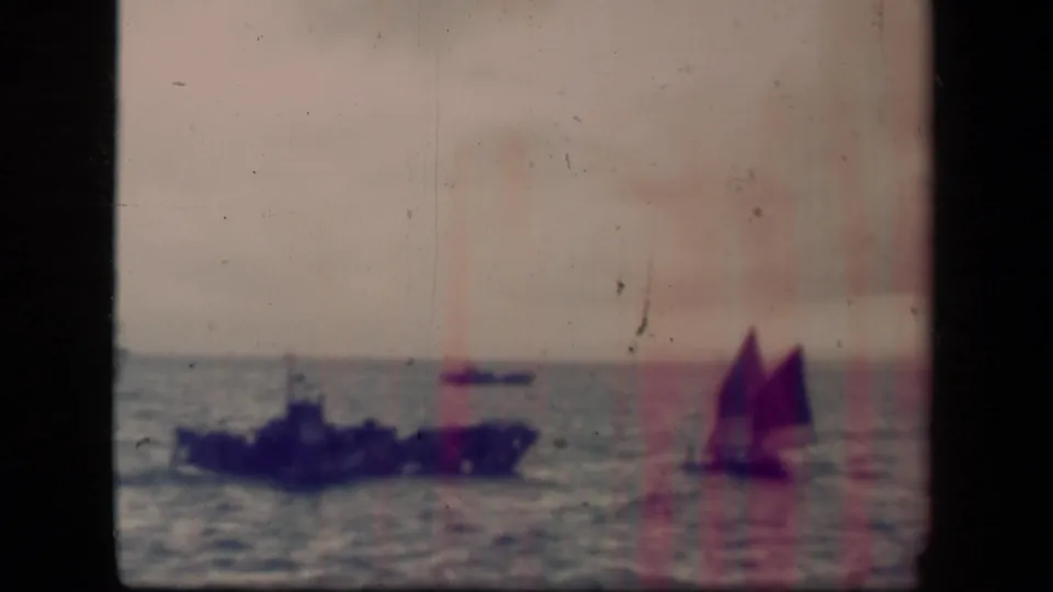 Faded 8mm Leyte Gulf 1944 frame showing a dark warship at left, a small distant craft, and a sailboat on calm open water.