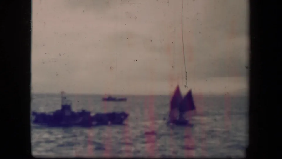 Leyte Gulf 1944 frame with a distant warship at left and a sailboat at right, softened by grain, scratches, and faded color.