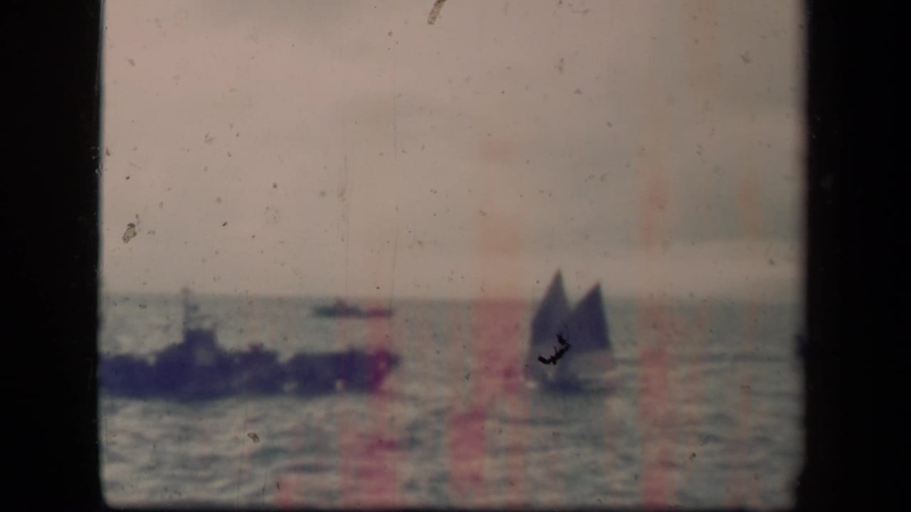 Distant ships on open water with hazy sky and visible film wear.