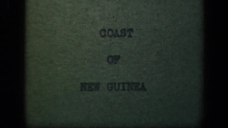 Centered "COAST OF NEW GUINEA" title card from the 8mm reel, surrounded by dark gate edges and faded color.
