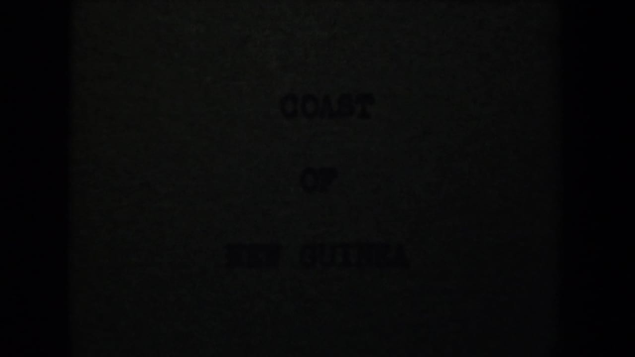 Underexposed 1944 8mm title card for Coast of New Guinea, partially obscured by dark frame edges and grain.