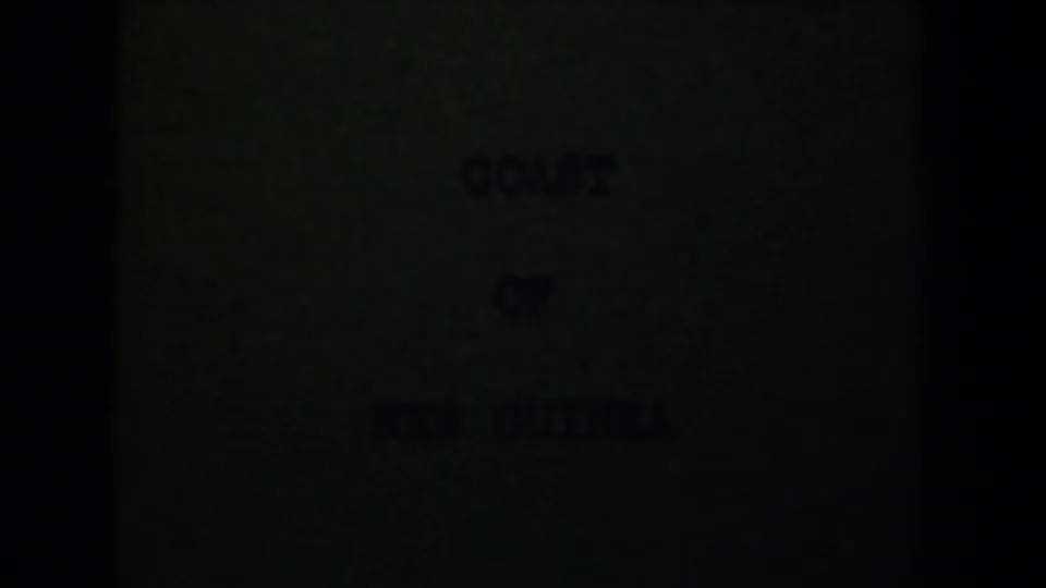 Underexposed 1944 8mm title card for Coast of New Guinea, partially obscured by dark frame edges and grain.