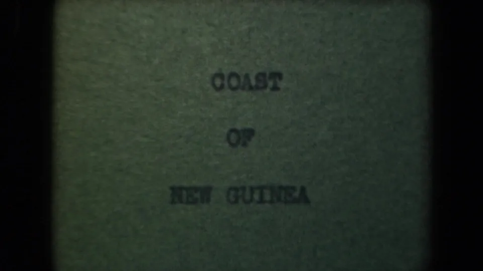 1944 8mm title card clearly reading Coast of New Guinea, with soft focus, grain, and dark vertical gate edges.