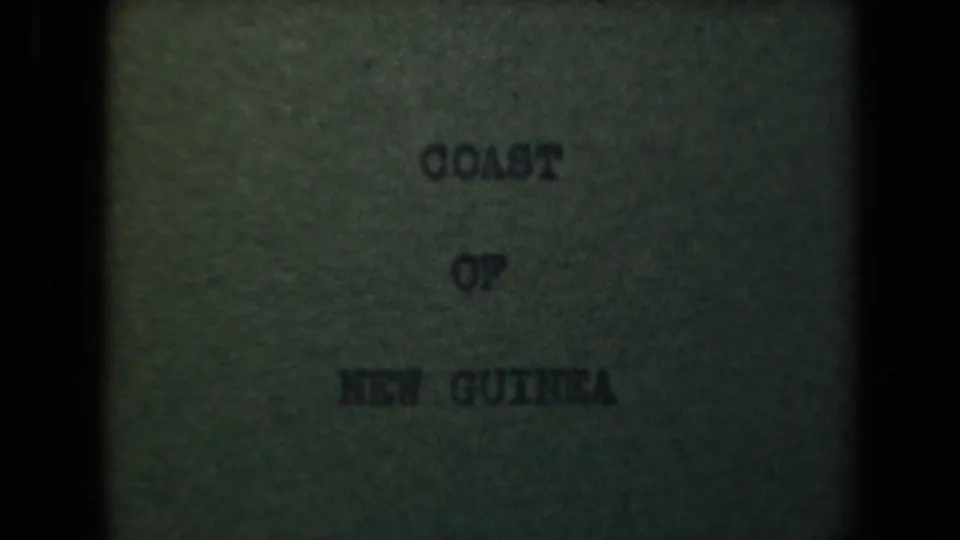 Grainy 1944 8mm frame holding the Coast of New Guinea title card, with dark gate edges and muted exposure.