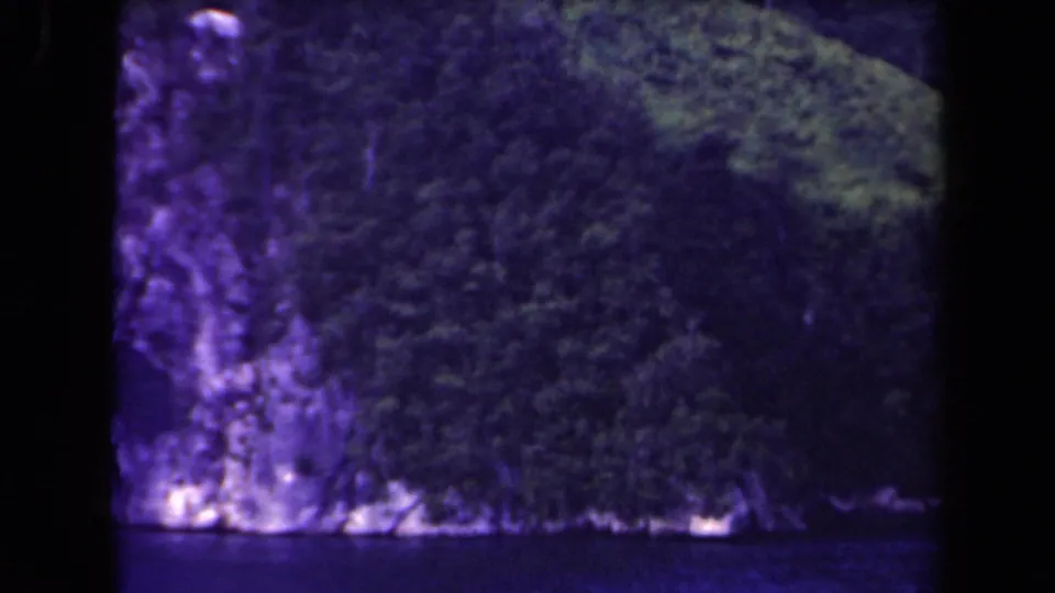 Boat-level view of a rugged Papua New Guinea shoreline with forested slopes and rocky cliff bases.
