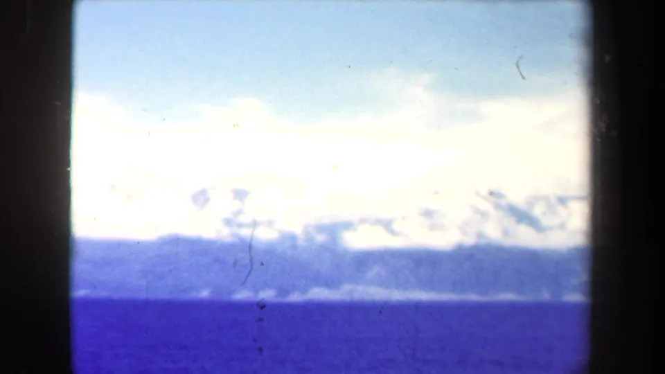 1944 Papua New Guinea 8mm aerial view of blue water, distant mountain ridges, and cloud cover within a dark film frame.