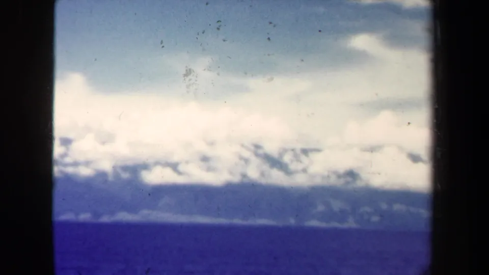 1944 Papua New Guinea aerial view with low clouds, distant mountainous shoreline, open water, and visible 8mm dust and scratches.