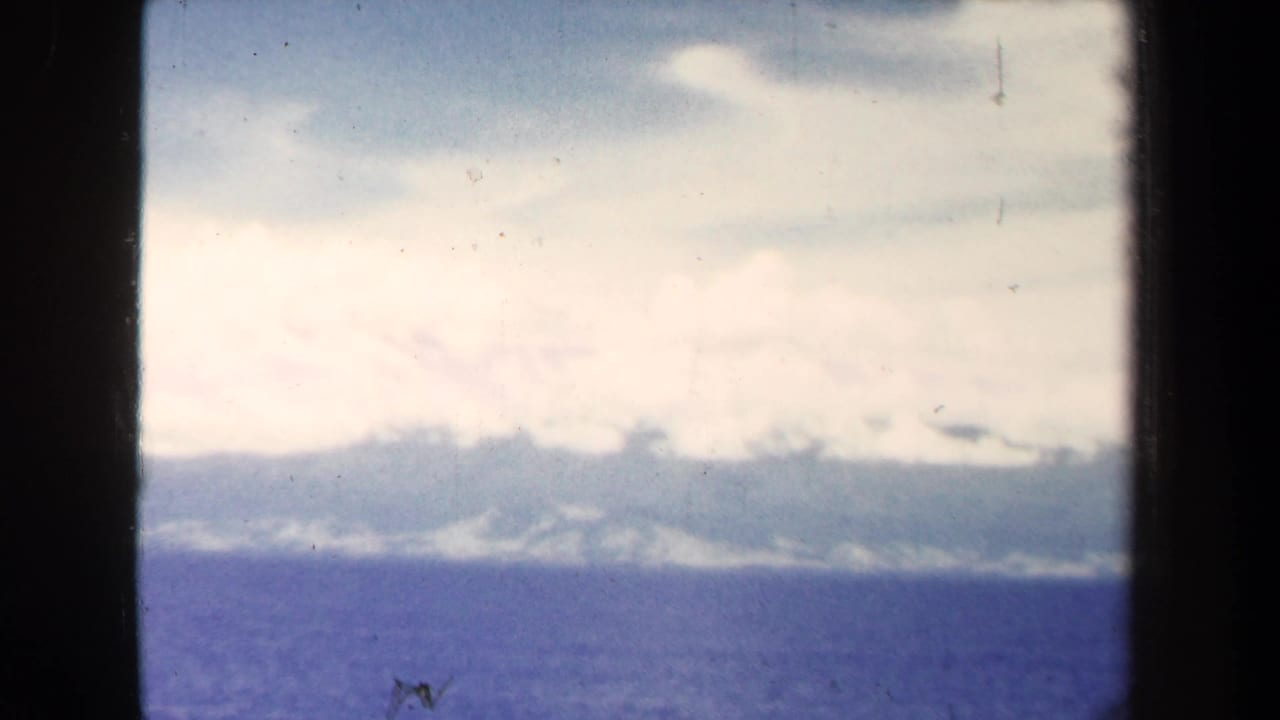 1940s 8mm view near Papua New Guinea showing blue ocean, hazy coast, and pale clouds from a shipboard perspective.