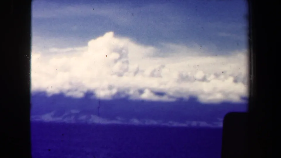 Vintage 8mm frame near Papua New Guinea with a cloud bank stretching over blue water and a low, hazy coastline.