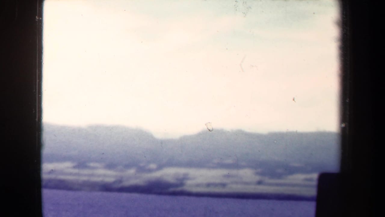 1944 Papua New Guinea 8mm frame showing a hazy mountain horizon beneath pale clouds, viewed through dark window-like borders.