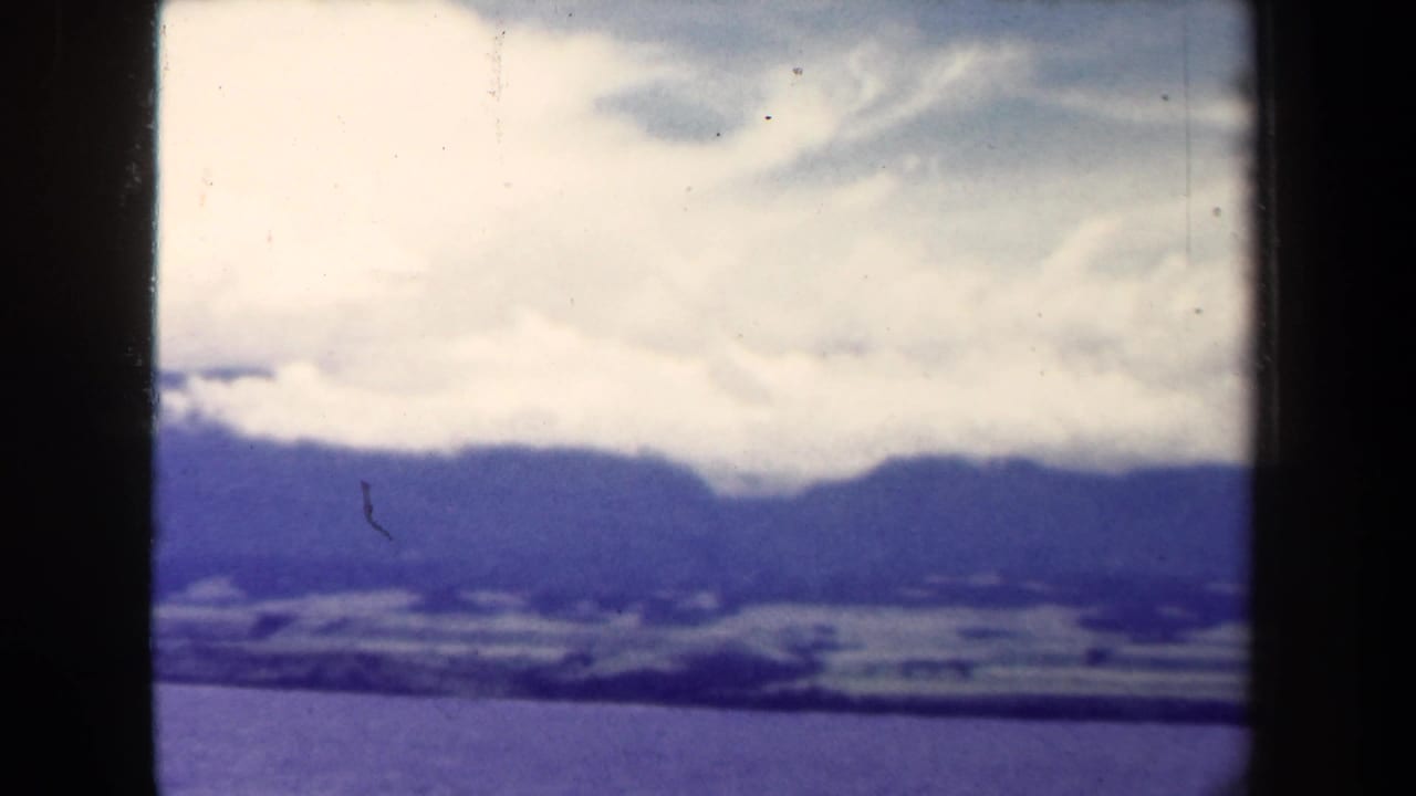 1944 Papua New Guinea 8mm view of a blue mountain range under bright cloud cover, framed by dark vertical edges.