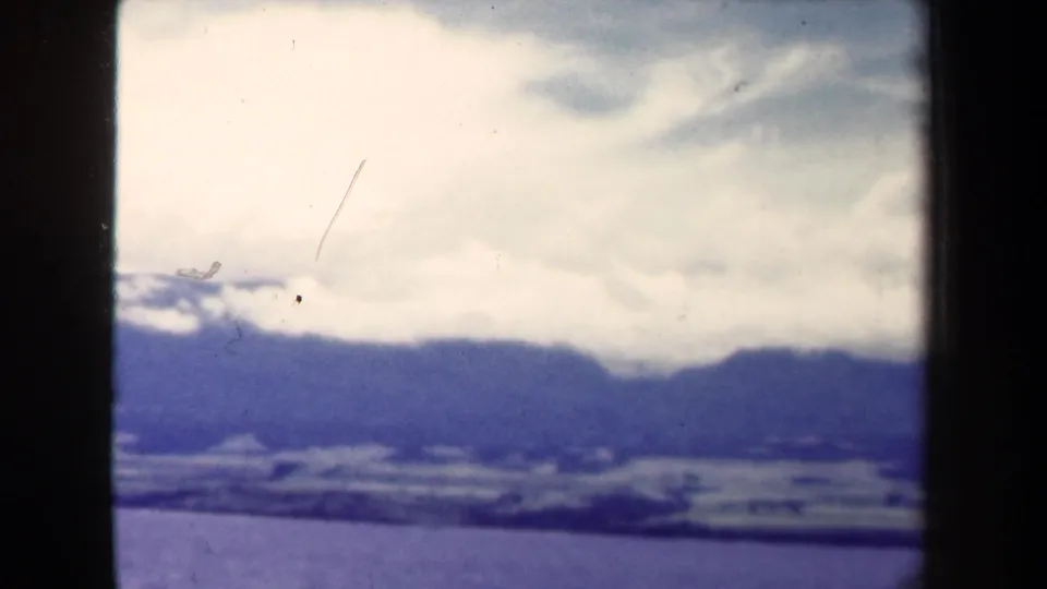 1944 Papua New Guinea 8mm frame with cloud cover over a distant blue mountain ridge and a dark foreground band.