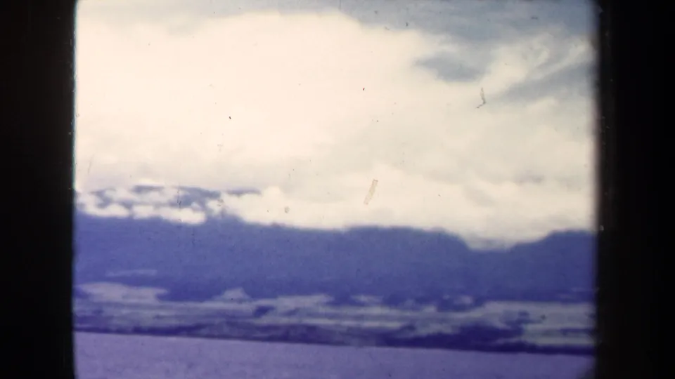 1944 Papua New Guinea 8mm view of a distant mountain horizon and bright cloud layer, bordered by dark film edges.