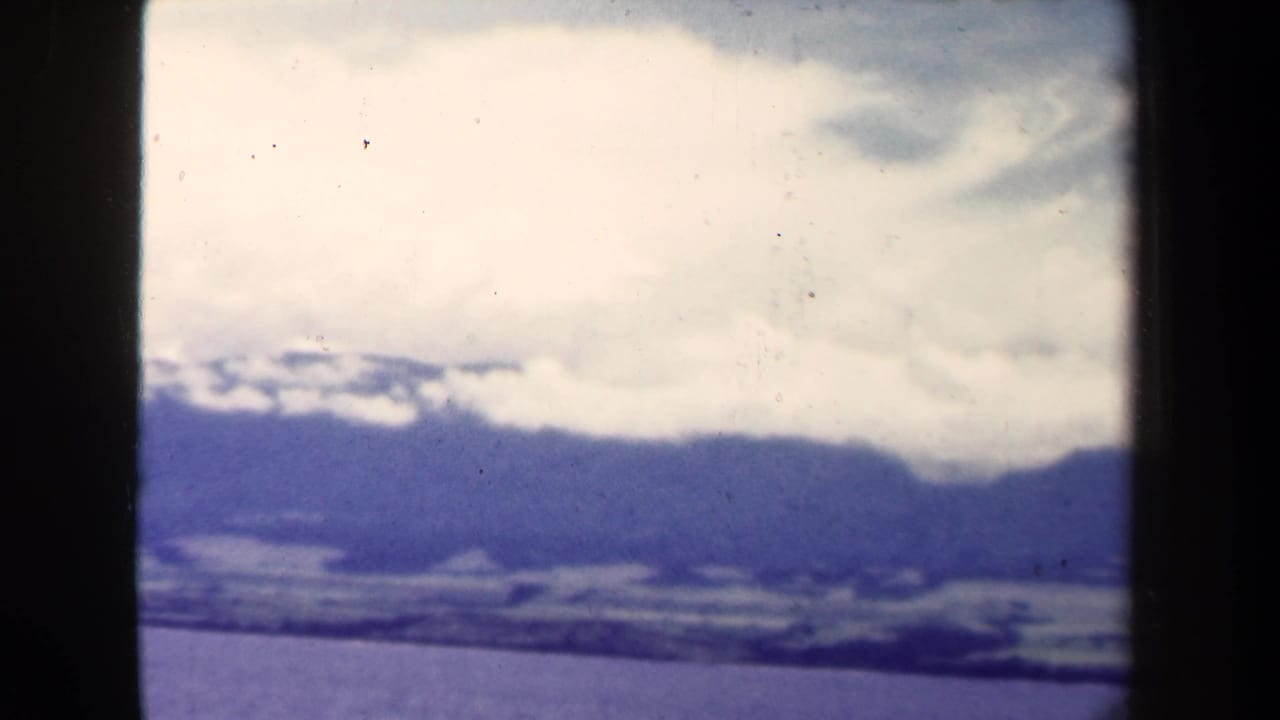 Distant mountain range beneath thick white clouds with dark film borders.