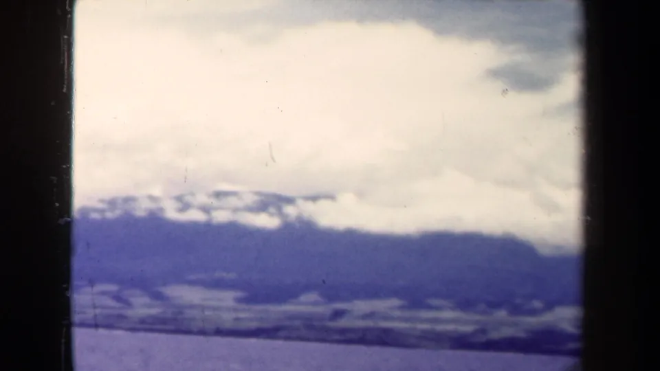 1944 Papua New Guinea 8mm frame with a distant mountain range, pale cloud cover, and visible scan borders.