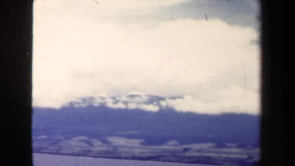 1944 Papua New Guinea 8mm frame showing a hazy mountain range under thick clouds with archival film texture.