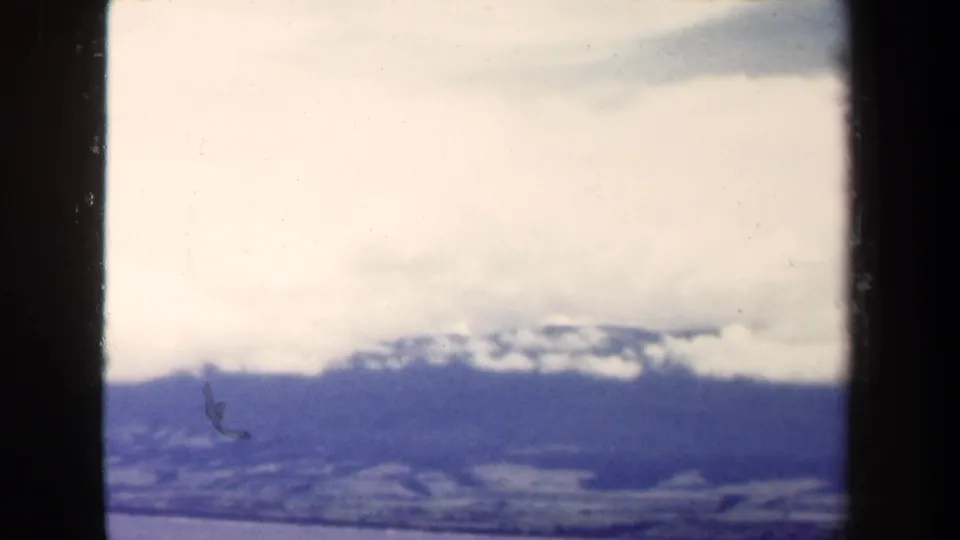 1944 Papua New Guinea 8mm frame with a blue-toned distant ridge, bright cloud cover, and small film marks.