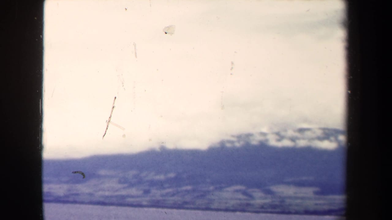 Distant Papua New Guinea mountain range partly obscured by clouds above ocean water, seen in worn 1940s 8mm footage.