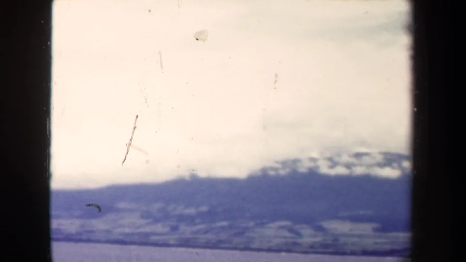 Distant Papua New Guinea mountain range partly obscured by clouds above ocean water, seen in worn 1940s 8mm footage.