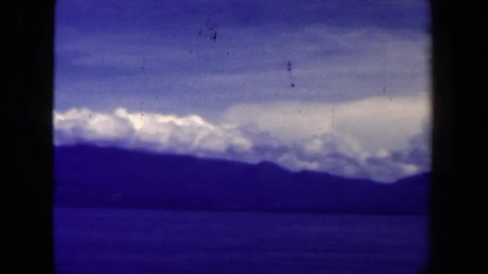 1944 8mm Papua New Guinea landscape showing a lake, dark mountain ridge, and layered clouds under a blue-purple sky.