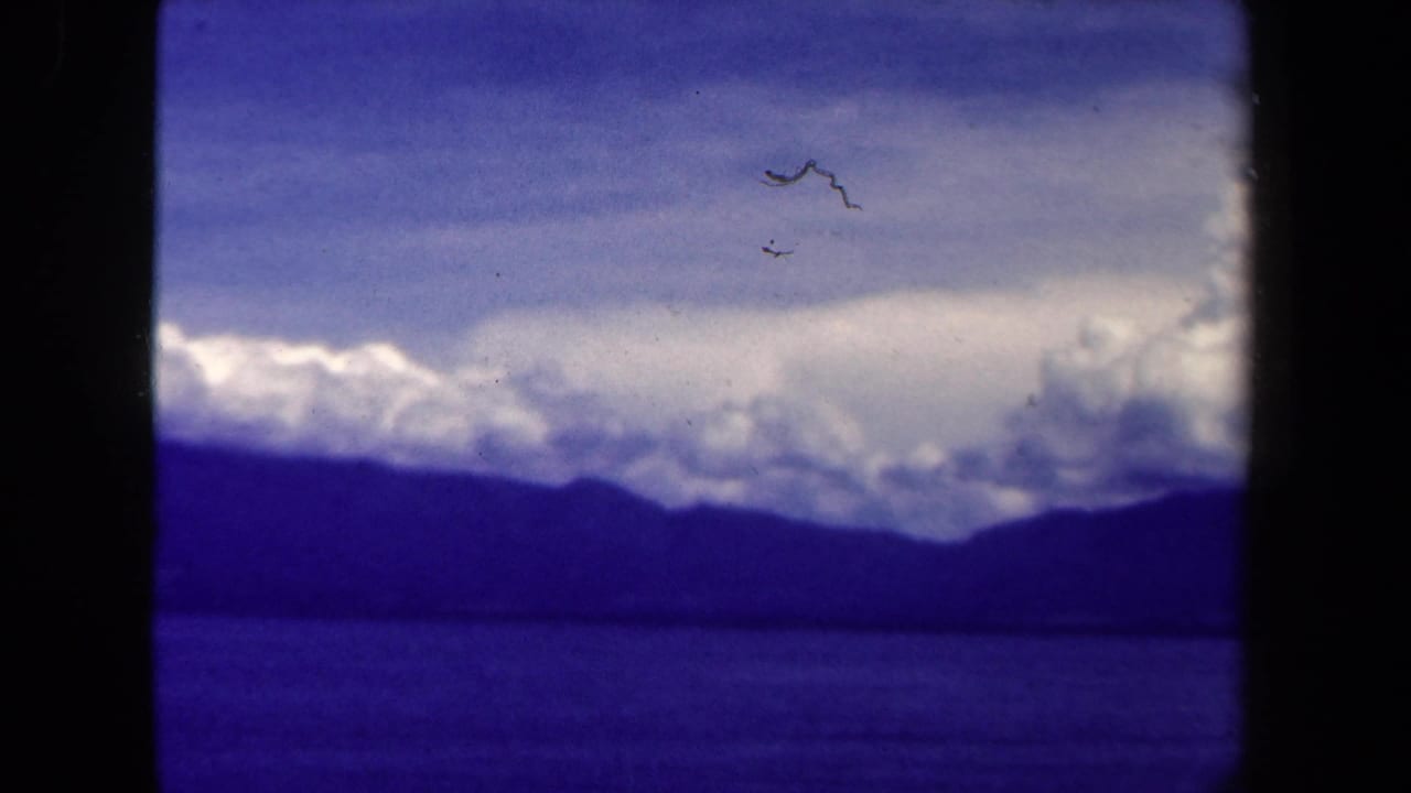 Clouds and distant mountains over a dark lake with film gate edges visible.
