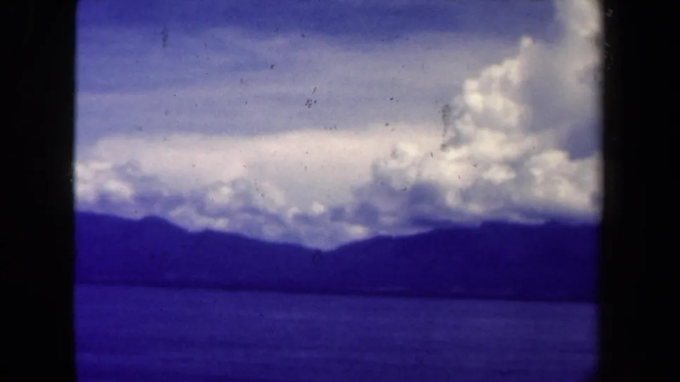 1944 8mm Papua New Guinea frame showing lake water, dark hills, and a large cloud mass under a tinted sky.