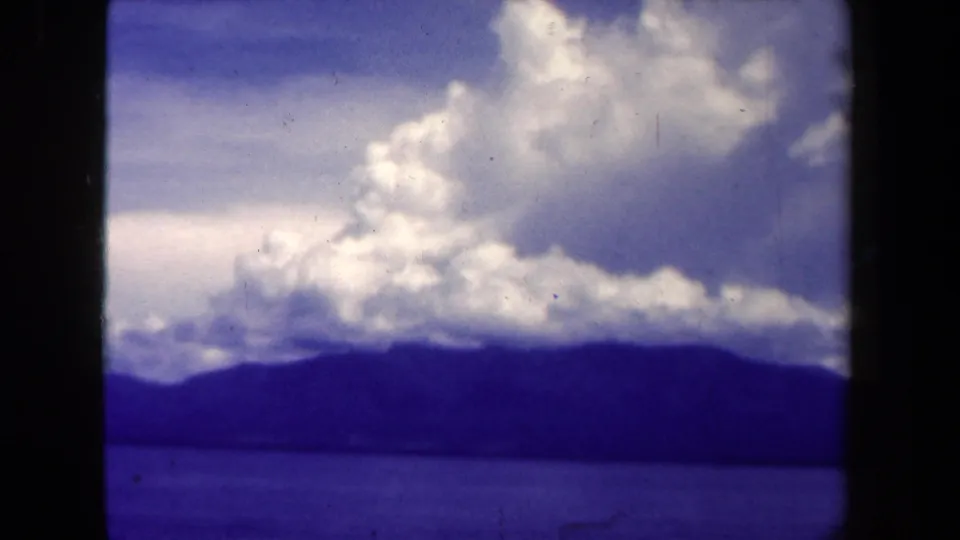 Final 1944 Papua New Guinea frame showing water, distant mountains, and a broad white cloud bank with visible 8mm grain.