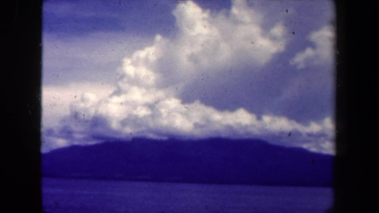Dark mountain ridge across bay water beneath a cloudy sky.
