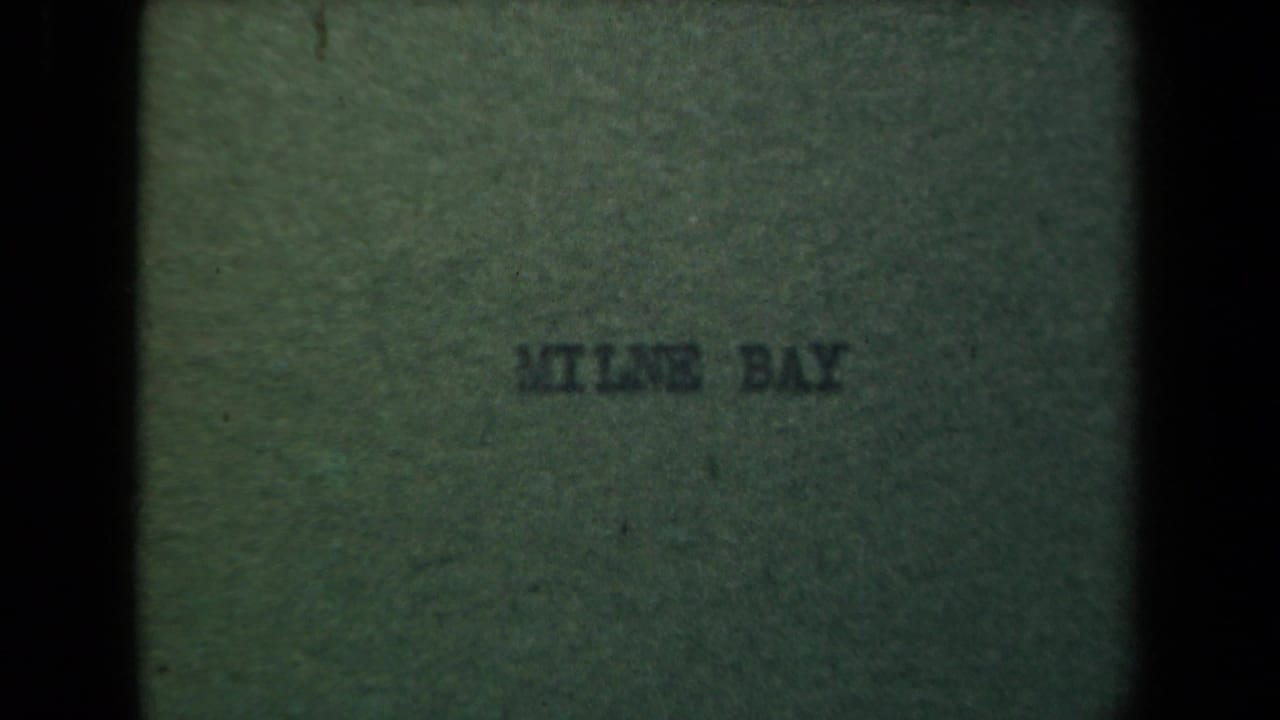 Green 8mm title card with faint centered text reading Milne Bay, showing film grain and soft focus.