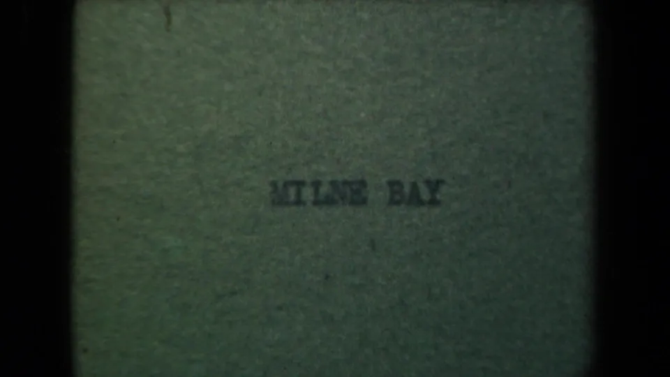 Green 8mm title card with faint centered text reading Milne Bay, showing film grain and soft focus.