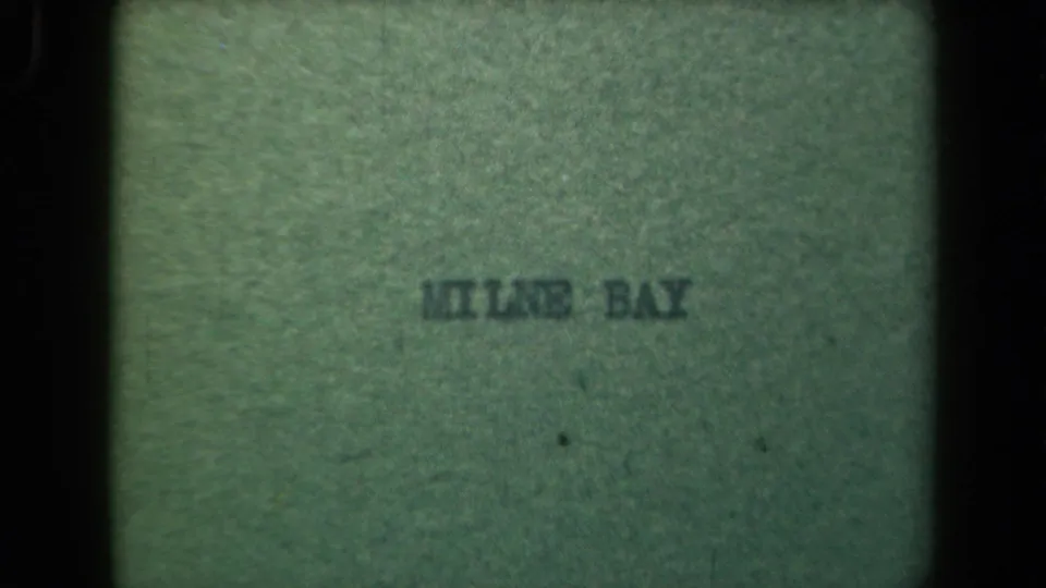 Faded green title-card frame from the Milne Bay clip, with dark printed text and visible 8mm grain.