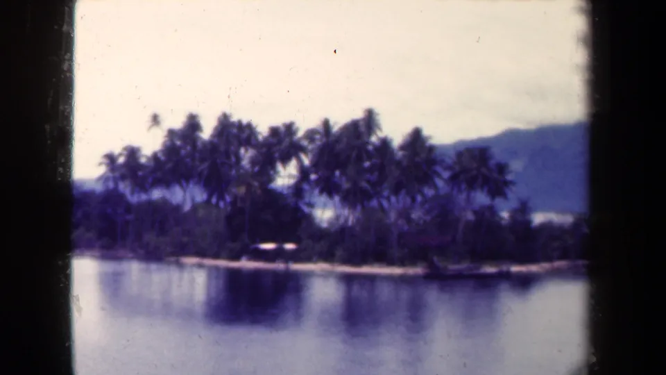 1944 Papua New Guinea 8mm frame showing a small palm island, still water, and distant mountains with a purple-blue film cast.