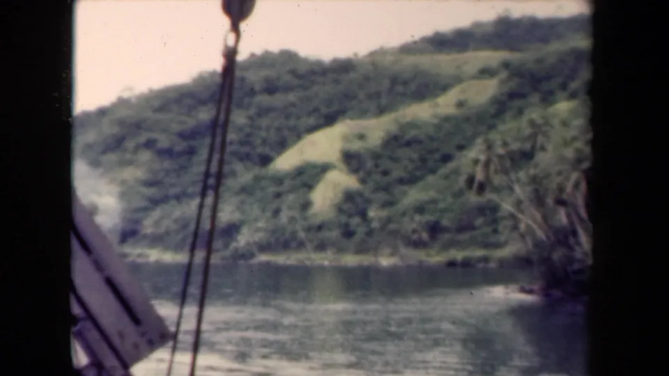 1944 Papua New Guinea frame showing boat rigging at left, calm water below, and green tropical hills along the shore.