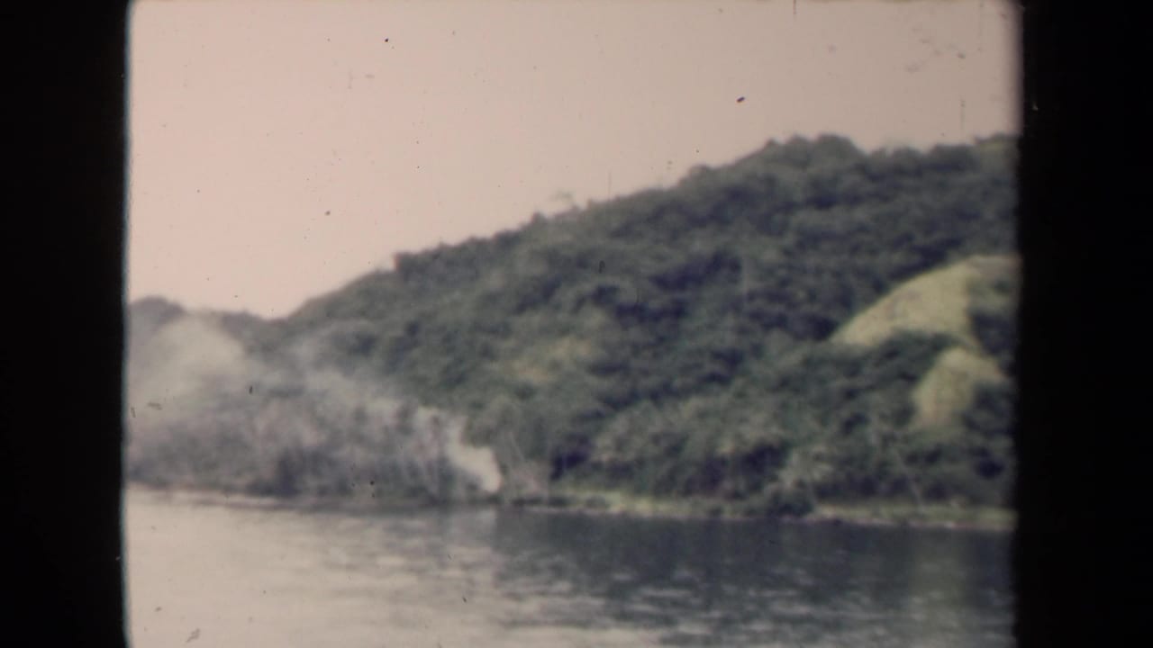 Calm river beside a forested hillside with pale sky and film frame edges.