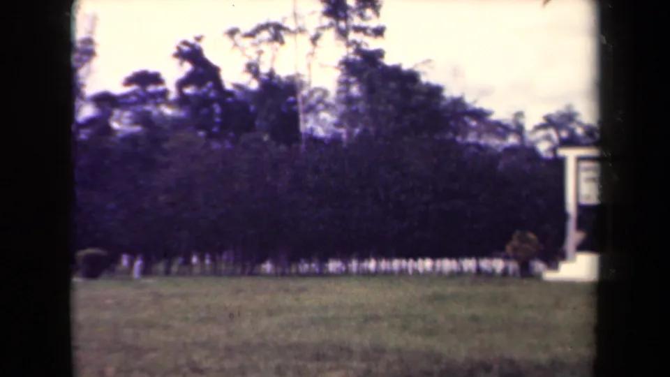 1944 Papua New Guinea home-movie view of a maintained grassy area and white sign structure near dense trees.