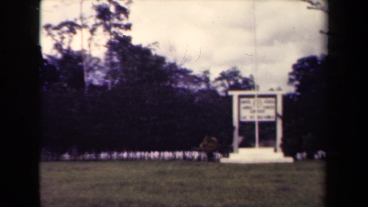 1940s Papua New Guinea 8mm frame showing a white sign structure on a lawn before dark tropical trees.