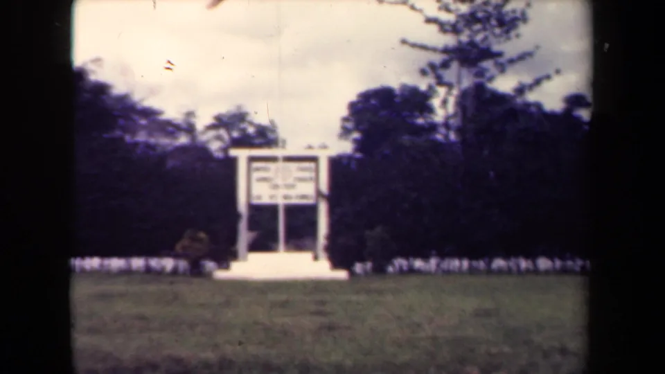Final 1940s Papua New Guinea frame keeps the distant white sign in view, with tropical trees and visible 8mm scan borders.