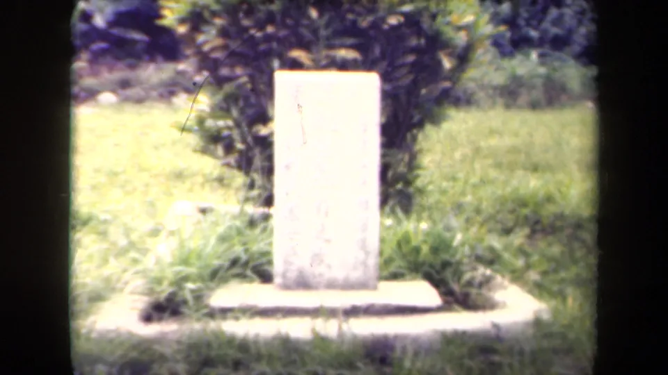 1940s Papua New Guinea footage appears to show a pale memorial stone set in grass with shrubs behind it.