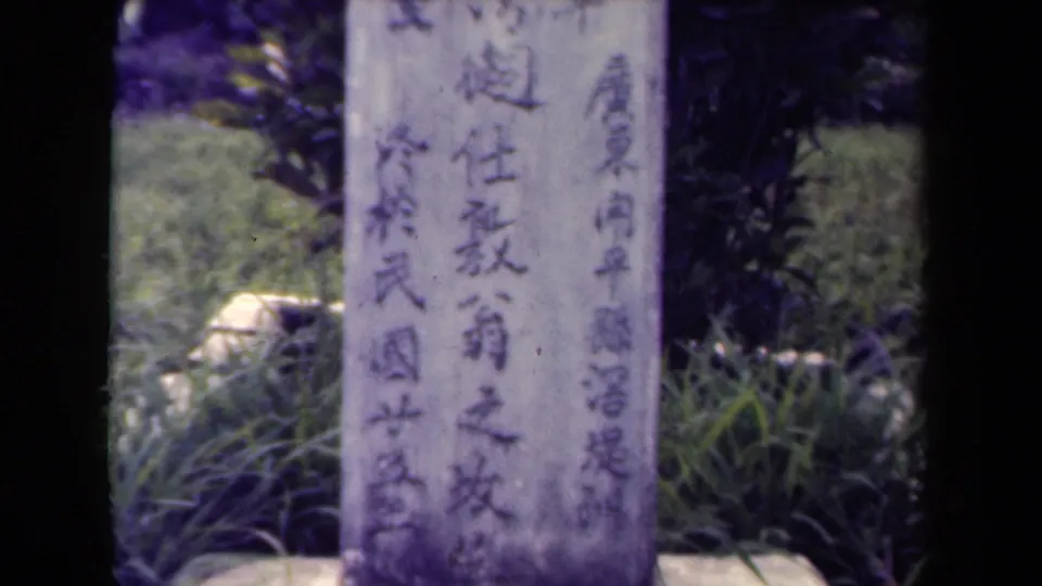 The final close frame shows the Chinese-inscribed memorial stone with grass and shrubs in the cemetery setting.