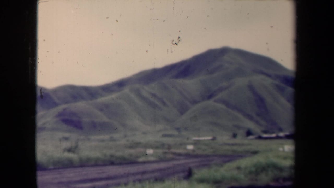 Mountain slope and valley floor with a dirt road curving through the foreground.