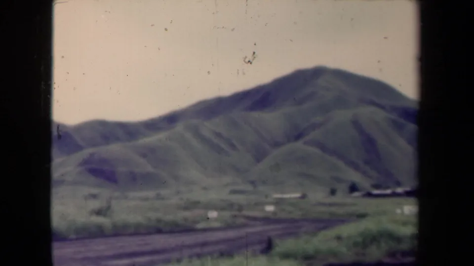 1944 Papua New Guinea rural landscape with rounded green hills, a pale sky, and an unpaved road crossing the lower frame.