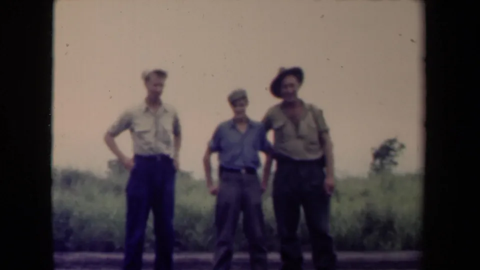 Three adult men in military-style clothing stand in a grassy Papua New Guinea setting in this 1944 home-movie frame.