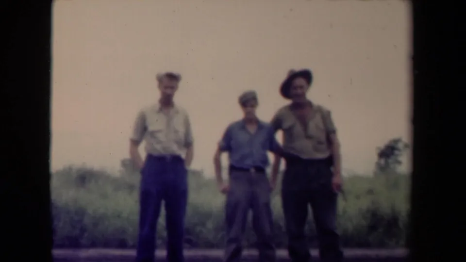 1944 Papua New Guinea 8mm frame of three adult men standing together, one wearing a wide-brimmed hat.