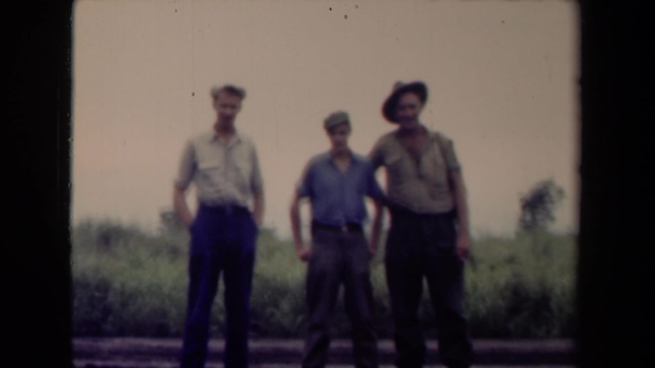 Three men stand beside a road with tall grass behind them.