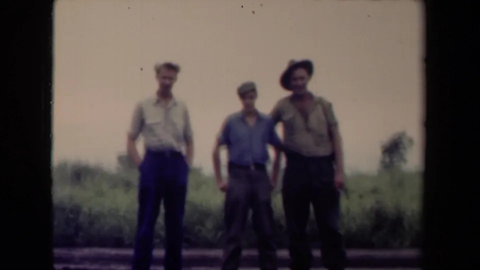 Three men in military-style clothing stand along a roadside in Papua New Guinea, filmed in soft 1940s 8mm color.